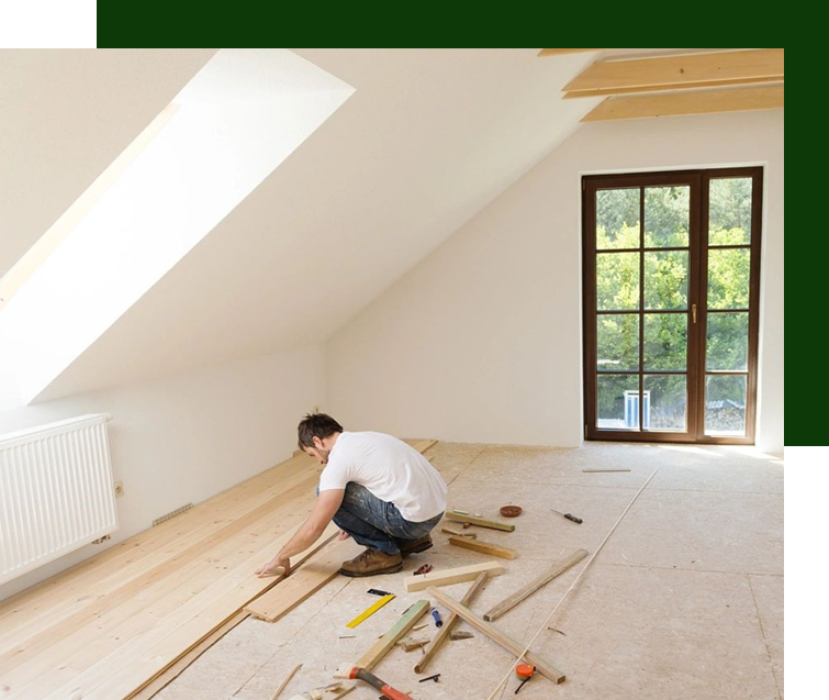 A man is working on a wooden floor in an attic.