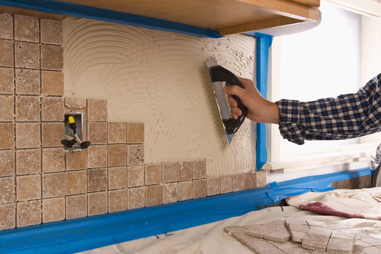 A person is sanding the wall of a kitchen.