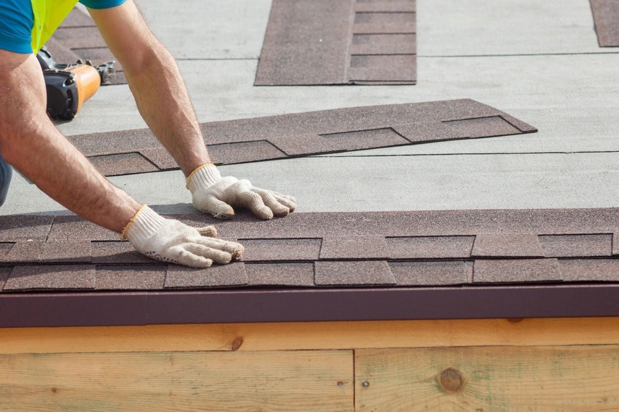 A person with gloves on is working on the roof of a house.